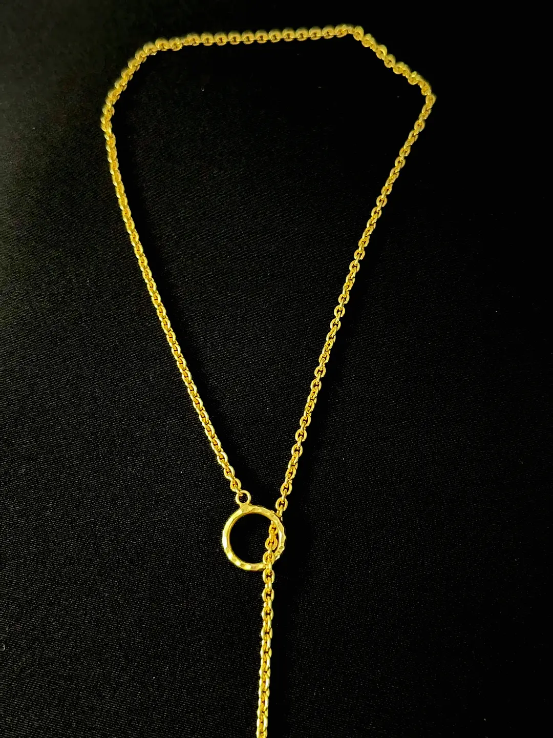 The Amrit necklace laid out, chain threading the hammered ring to the solid teardrop