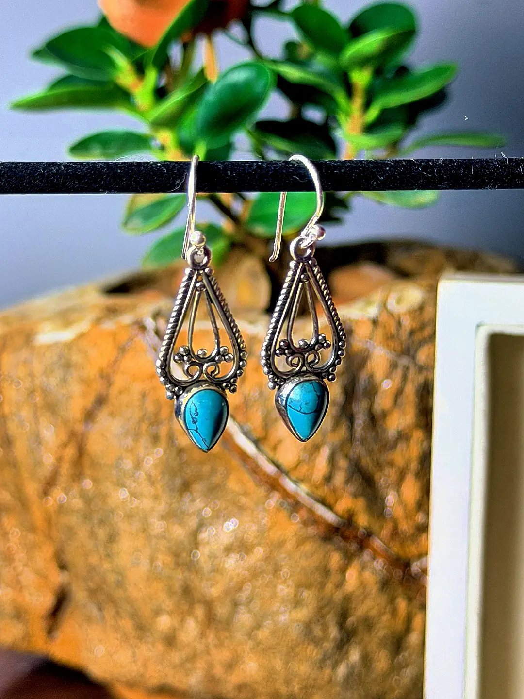 Firoza earrings photographed hanging against stone and foliage