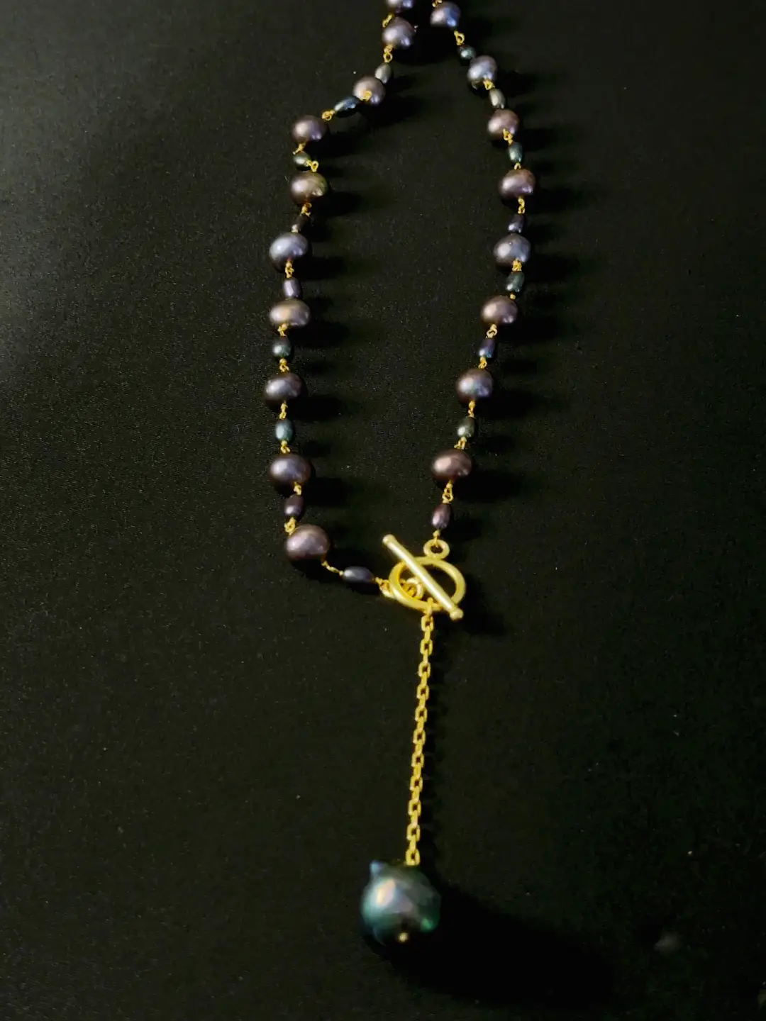 The Nisha strand laid out, peacock-black pearls wired along the gold chain