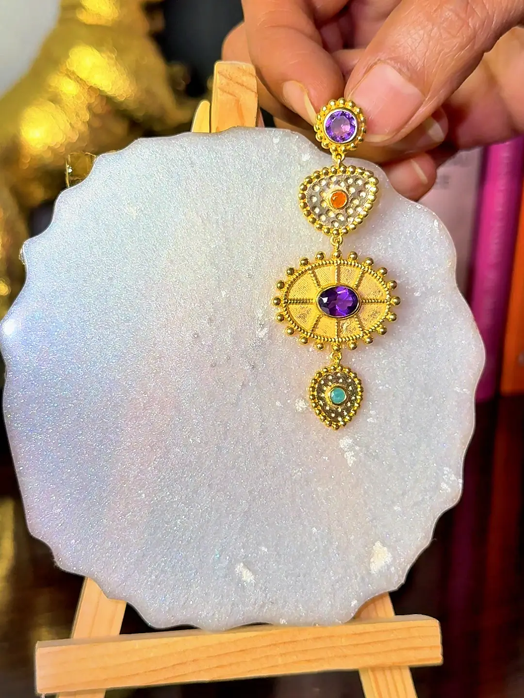 A single Surya earring held in the hand, showing its drop length and scale