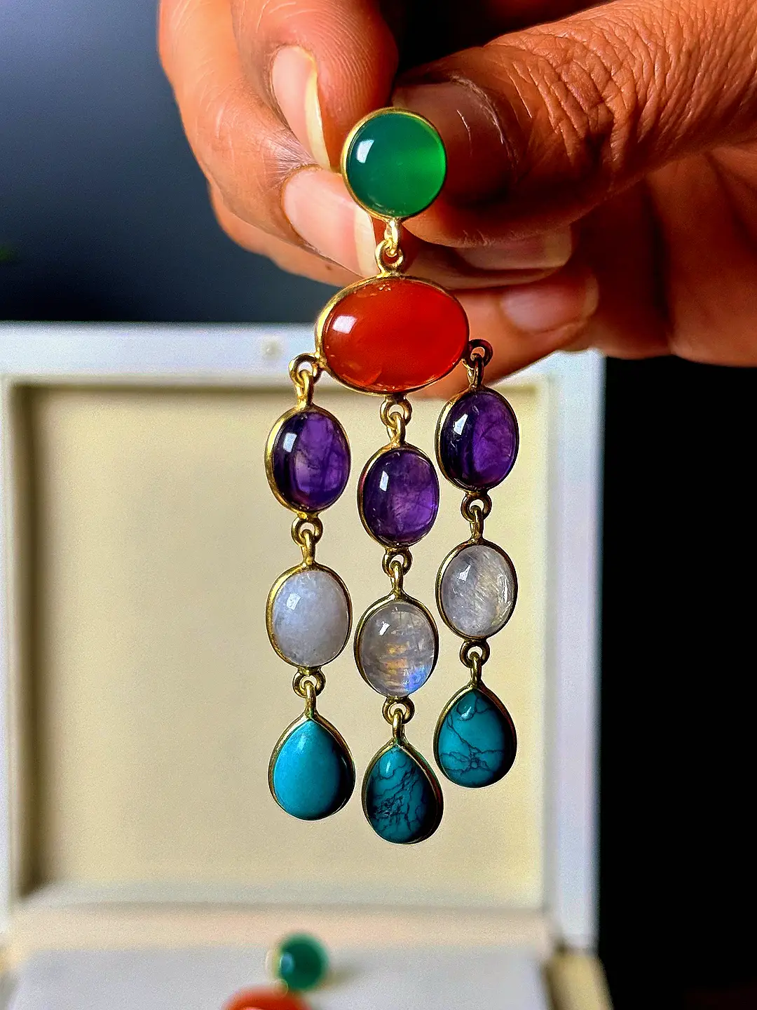 A single Utsav earring held in the hand, showing its drop length and three strands